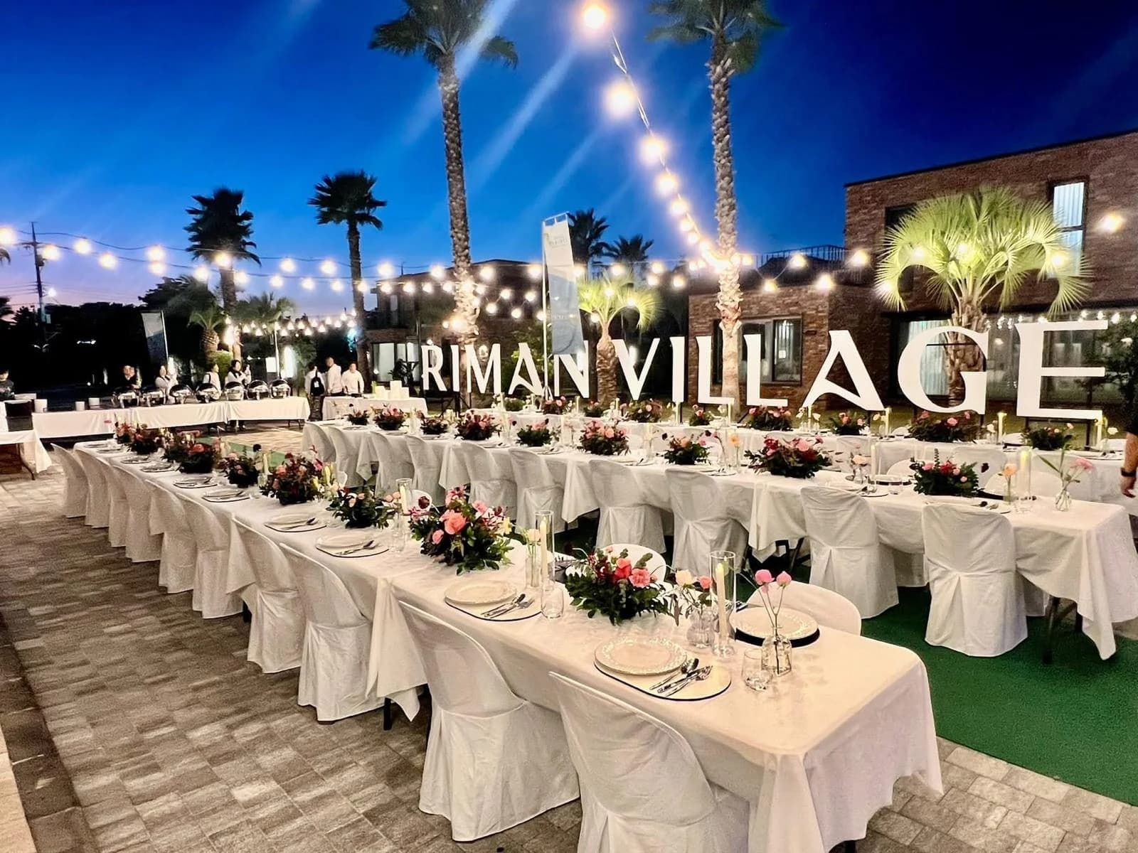 Tavoli allestiti su una terrazza con insegna RIMAN Village.